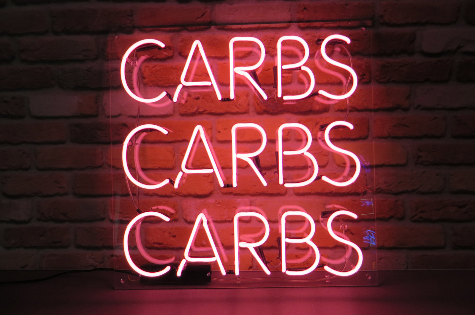 CARBS CARBS CARBS' pink neon sign. Real glass neon mounted on clear acrylic panel.