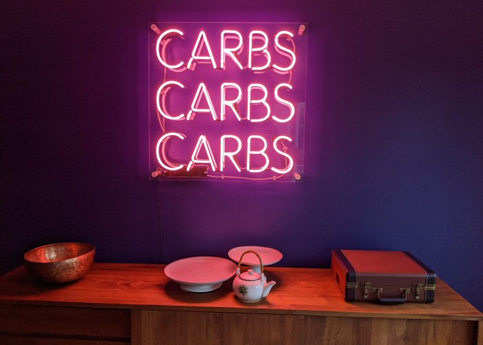 CARBS CARBS CARBS' pink neon sign. Real glass neon mounted on clear acrylic panel.