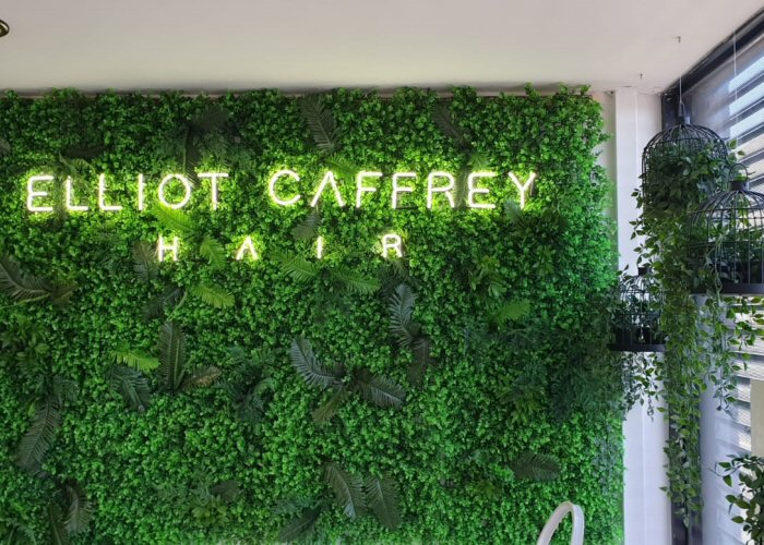 ELLIOT CAFFREY HAIR' white neon sign. Real glass neon fitted directly onto artificial foliage.