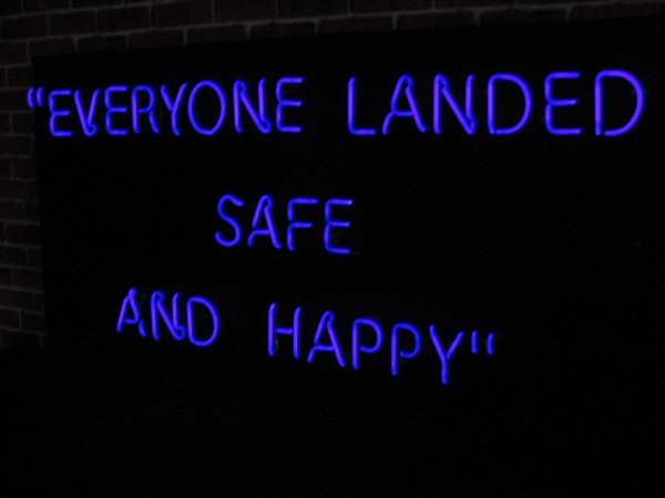 EVERYONE LANDED SAFE AND HAPPY' UV neon. Real glass neon fitted onto a black acrylic panel.