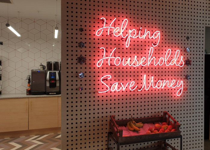Helping Households Save Money' pink neon sign. Real glass neon fitted directly onto the wall.