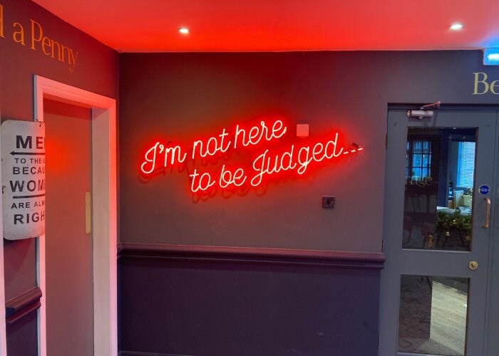 I'm not here to be judged' red neon sign. Real glass neon fitted directly onto wall.