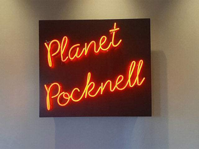 Planet Pocknell' orange neon sign. Real glass neon mounted on to client's own wooding backing.